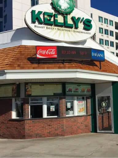 Exterior of Kelly’s restaurant with menu signs, digital clock, and soda advertisements above the entrance.
